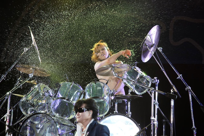 ドラムを叩きながら激しく水をまき散らすYOSHIKI。手前はToshI。
