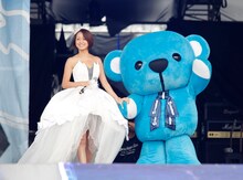 鈴木亜美。右はa-nationのマスコットキャラクター・Blue Teddy。