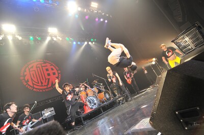 團長の無茶ぶりに応え、打点の高いバク宙を決める石鹸。ステージの左右ではメンバーの港カヲル（写真右端）とバイト君（写真左端）がまじまじとみつめている。