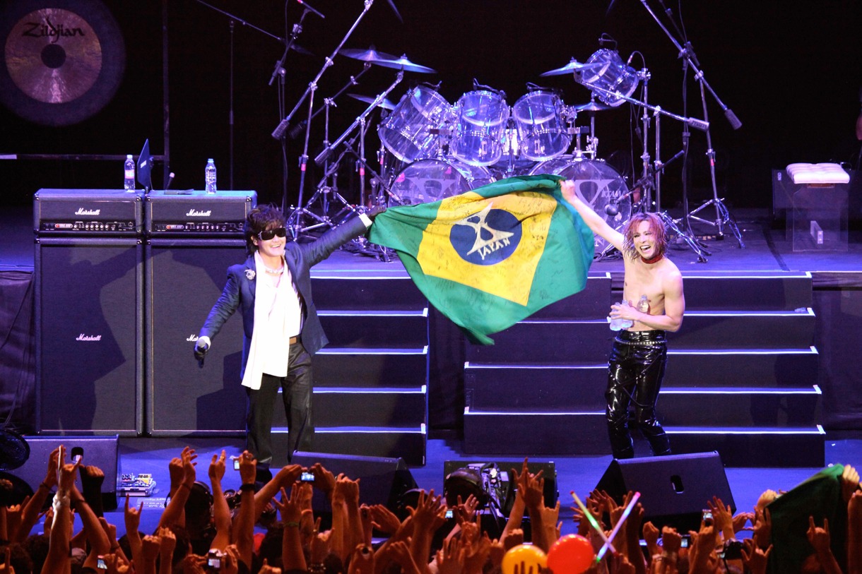 ファンから届けられた寄せ書き入りのブラジル国旗を仲良く掲げるToshI（写真左）とYOSHIKI（右）。