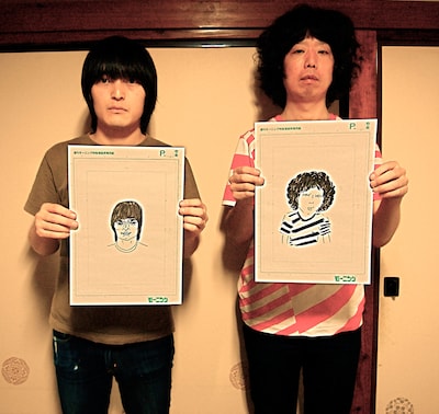 写真左から大橋裕之、坂本慎太郎。手にしているのはお互いに描きあった似顔絵。（撮影：ミチシタシンスケ）