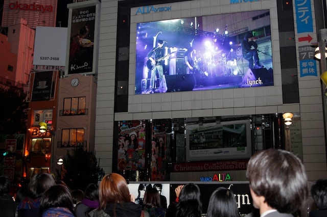 大勢のファンが過去のライブ映像を見つめる。