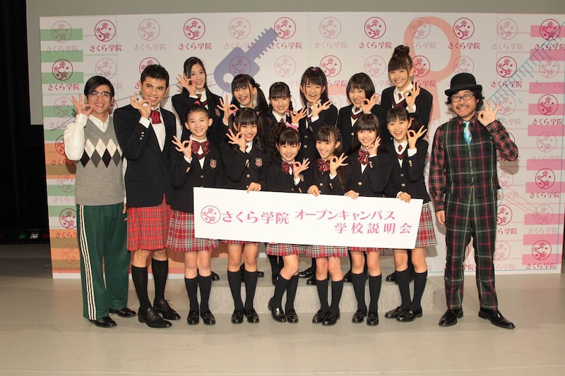 写真は囲み取材の様子。倉本美津留校長（写真右端）、メンバーと同じ衣装で体験入学した小島よしお（写真左から2番目）も一緒に記念撮影。