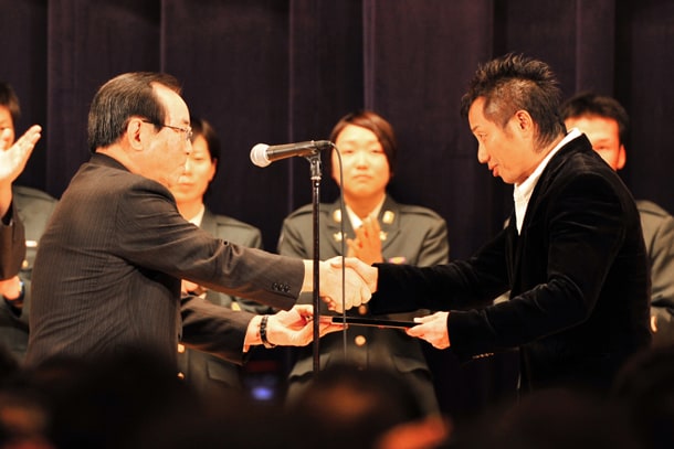 一川防衛大臣（写真左）と握手を交わす長渕剛（写真右）。