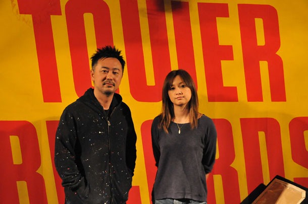 タワーレコードの看板前で記念撮影する伴都美子（写真右）と大渡亮（写真左）。