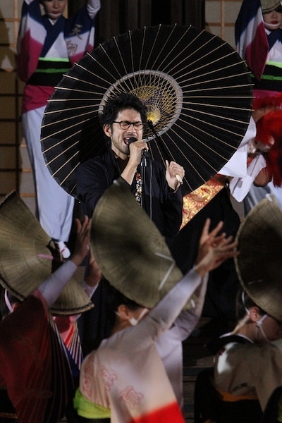 踊り子に囲まれ熱唱する平井堅。