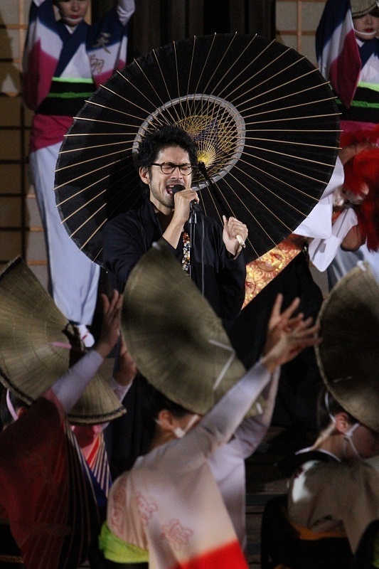 踊り子に囲まれ熱唱する平井堅。