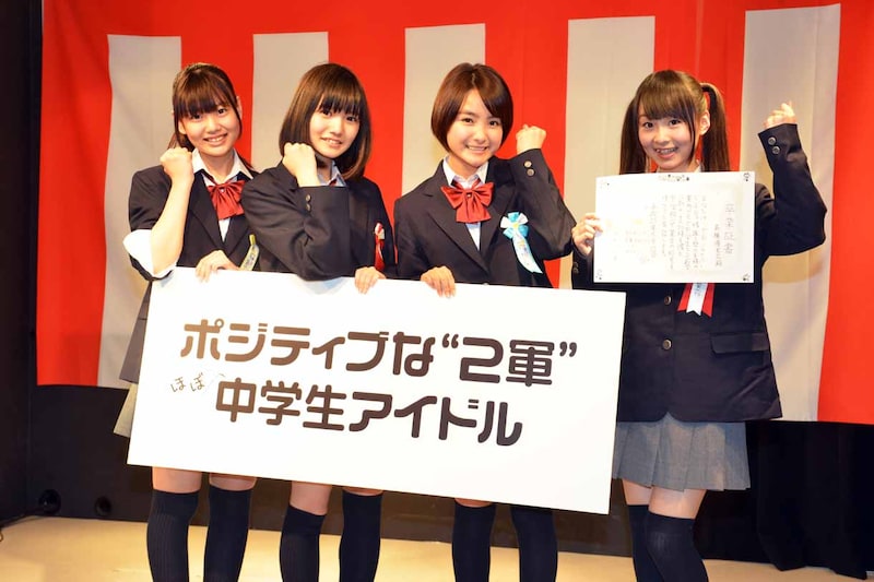 新キャッチフレーズが記されたボードを持つ田尻あやめ、荒川ちか、葵わかな(左から)と、卒業証書を手にした高橋優里花(右)。