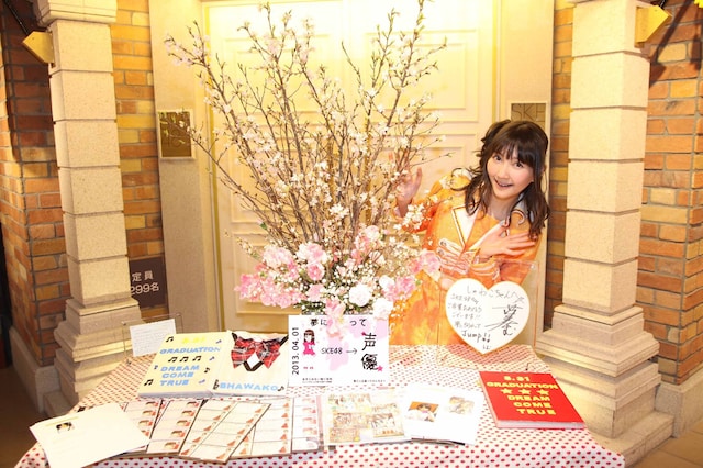 卒業を祝う品々の前で記念撮影する秦佐和子。（C)AKS