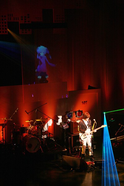 スクリーンに投影されたエネと共演するじん（自然の敵P）（撮影：Kobayashi TAXI）。