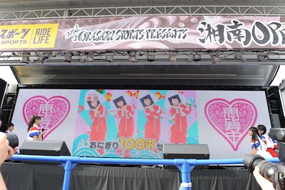 ステージ上のスクリーンで先行上映されたサークルKサンクスのCM。メンバーはおにぎりのかぶりものに挑戦している。