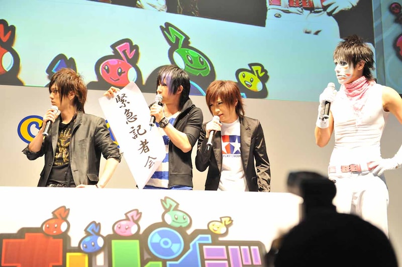 歌広場淳は「緊急記者会見」と書かれた紙を手に開発者に詰め寄る。