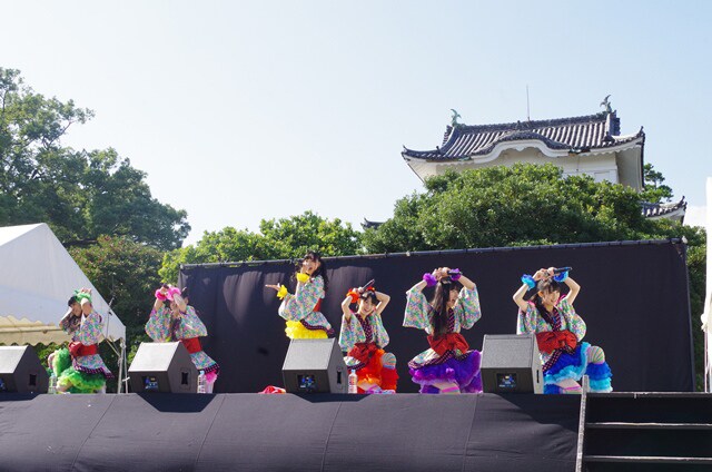 金の鯱がきらめく名古屋城をバックに歌うチームしゃちほこ。