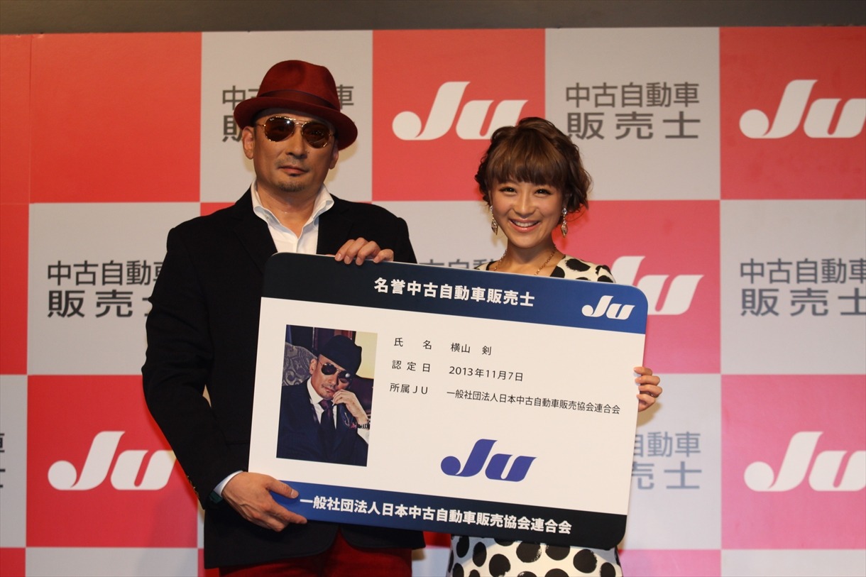 名誉中古自動車販売士の認定パネルを持つ横山剣と鈴木奈々。