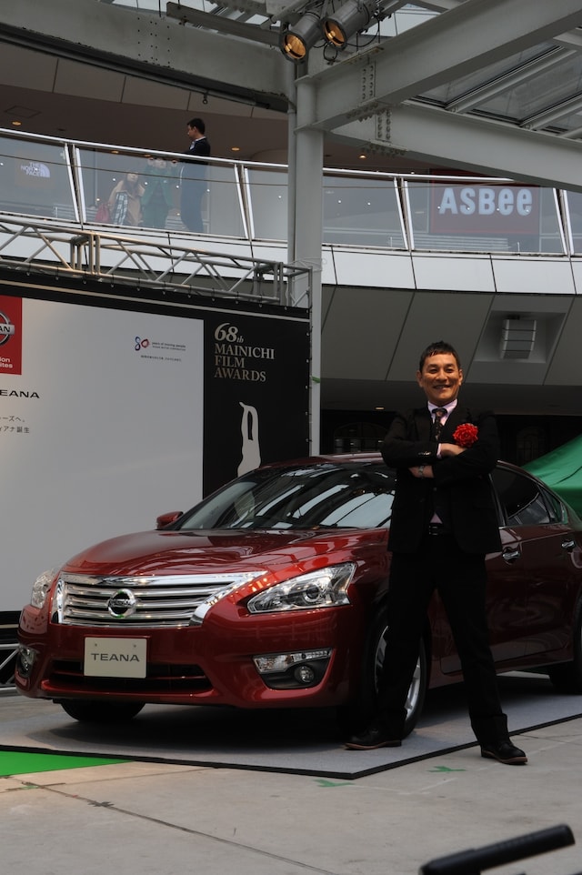 「第68回毎日映画コンクール」男優助演賞の副賞として贈られた「新型ティアナ」の前でポーズをきめるピエール瀧。