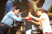 「第二回亀田杯 ベース選手権大会」のグランプリ、山本修也にトロフィーを渡す亀田誠治。