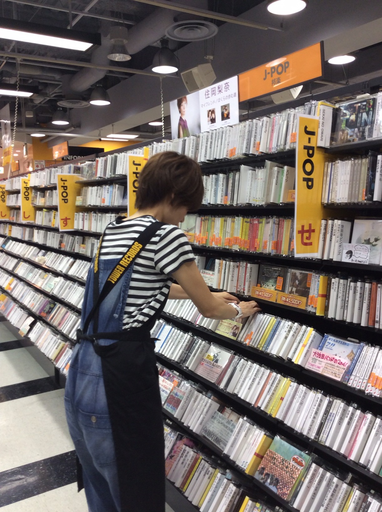 店内業務を体験する住岡梨奈。販売コーナーのCDの陳列を行っている。