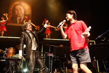 矢野水を持ってステージに上がった堀込泰行（右）。