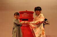 子供の年賀状投函をサポートする秋元真夏（右）。