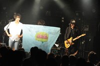 ファンからもらったフラッグを羽織る小林禄与（G, Syn, Per）。