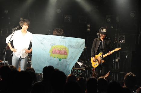 ファンからもらったフラッグを羽織る小林禄与（G, Syn, Per）。