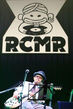 「RCMR（ラーメンカレーミュージックレコード）」のロゴをバックに歌う奥田民生。（撮影：山本倫子）