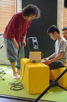 子供たちのオリジナル楽器にアドバイスするU-zhaan（左）。