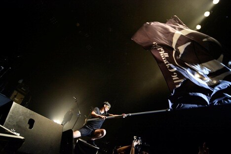 バンドの特大フラッグを振るドラゴンチャレンジ(Dr)。(撮影:小川舞)