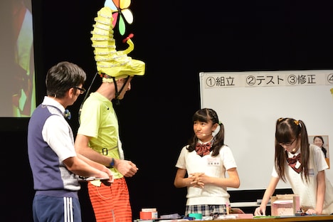 流暢な英語でジョセフ・テイムと会話する日高麻鈴と、その横で黙々と作業を続ける吉田爽葉香。