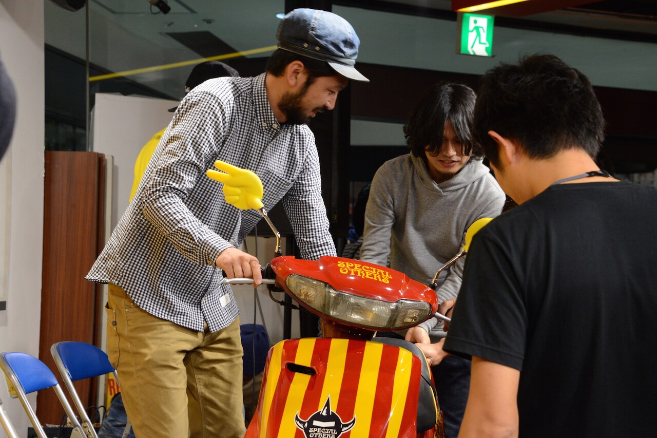 スクーターをステージに搬入するスペアザメンバー。