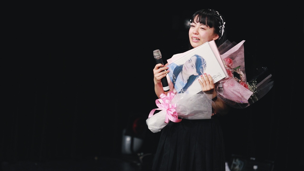 ファンが用意した花束とフォトアルバムを手にする宇佐美萌。（写真提供：AqbiRec）