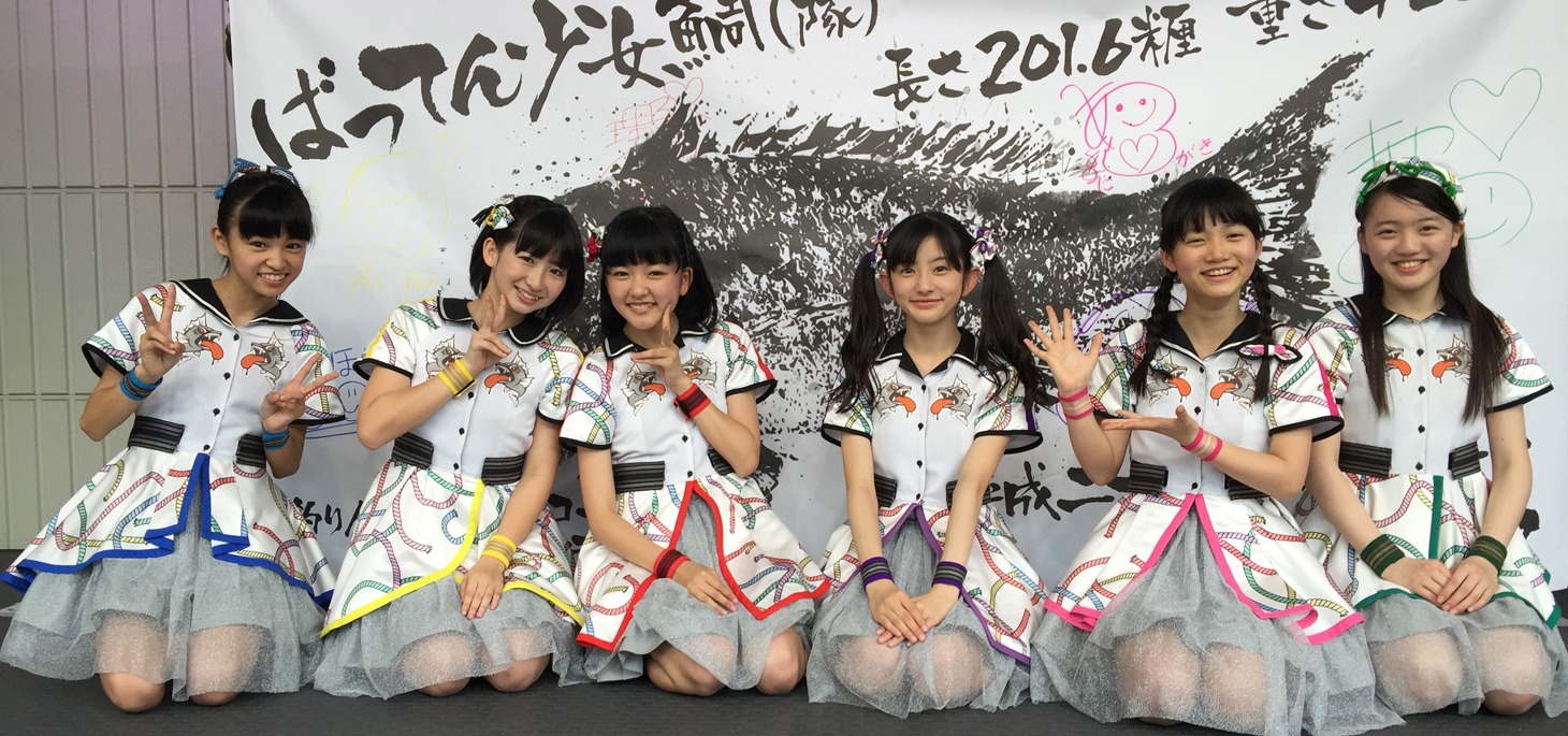「ばってん少女鯛（隊）」をバックに記念撮影するばってん少女隊。（写真提供：ビクターエンタテインメント）