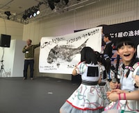 巨大な「ばってん少女鯛（隊）」に驚く西垣有彩（右端）。（写真提供：ビクターエンタテインメント）