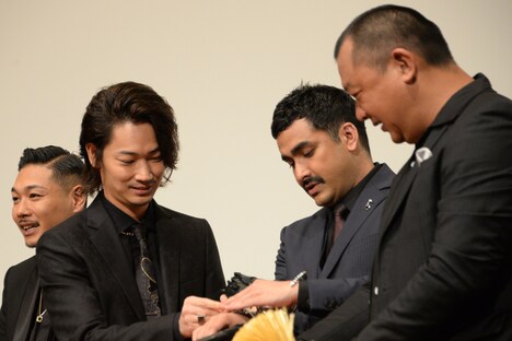 植野行雄（デニス）に手錠をはめる綾野剛（左から2番目）。