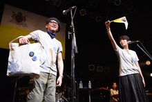 自身もお気に入りのTWEEDEESオリジナルグッズを紹介する沖井礼二（左）と、旗を振って盛り上げる清浦夏実（右）。