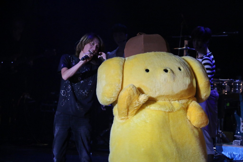 ポムポムプリン（右）と寄り添う角松敏生（左）。(c)SANRIO