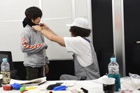 ZEN-LA-ROCK（右）が持参したNEMESのロンTを試着するジョー（左）。ZEN-LA-ROCKはこのあと「お年玉」としてロンTをジョーにプレゼント。