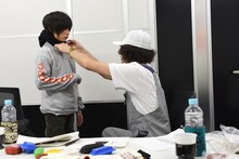 ZEN-LA-ROCK（右）が持参したNEMESのロンTを試着するジョー（左）。ZEN-LA-ROCKはこのあと「お年玉」としてロンTをジョーにプレゼント。