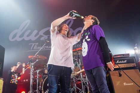 SUGA（Vo, G）にシャンパンを飲ませるJOJI（B, Vo）。（Photo by HayachiN）