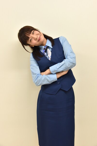 銀行員のOL衣装で首をかしげてポーズをとる吉澤嘉代子。
