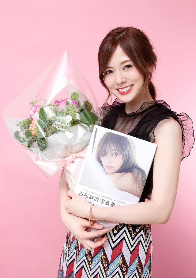 花束と「パスポート」を抱えて笑みを浮かべる白石麻衣（乃木坂46）。
