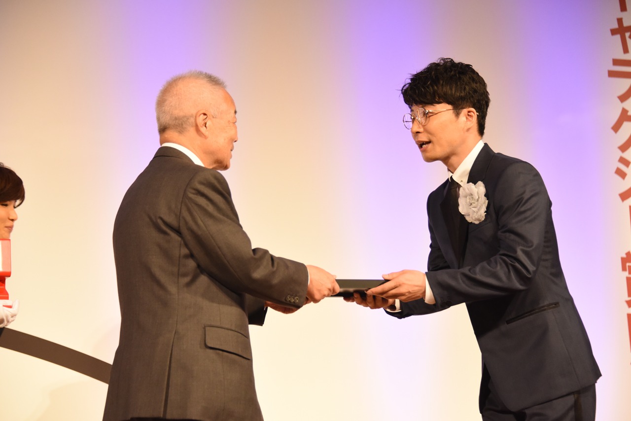 橋本隆氏から盾を受け取る星野源（右）。