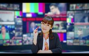 angela「全力☆Summer!」ミュージックビデオより、ニュースキャスターになったatsuko（Vo）。