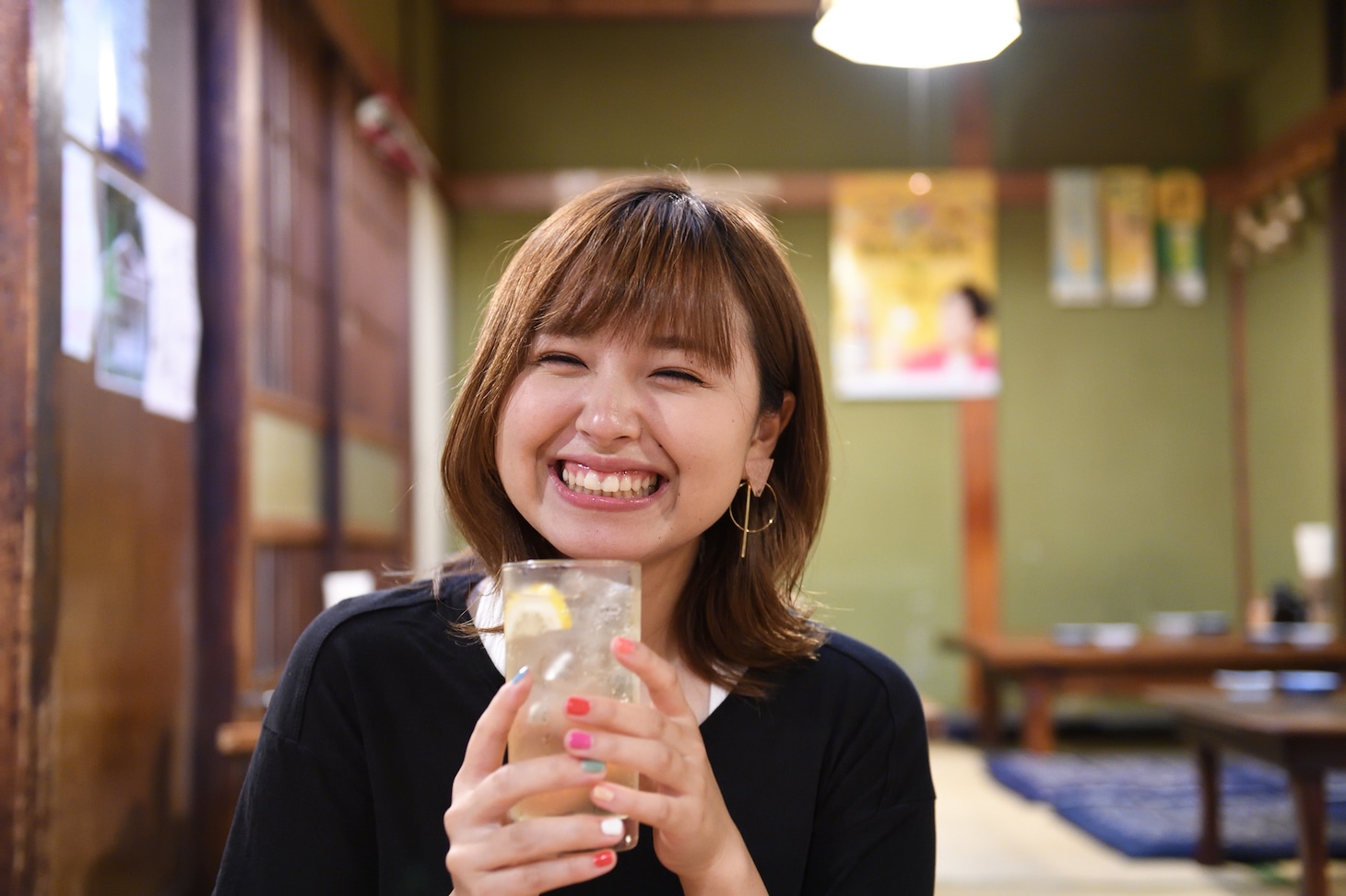 脇田もなり新連載「「名酒場IN THE CITY」」のワンカット。ハイボールを手に満面の笑みを浮かべる脇田もなり。（撮影：石川啓次）