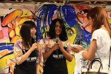 布製おにぎりを手渡すしばたありぼぼ（B, Vo）。