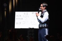 山出愛子と岡田愛の反復横跳び対決の結果を書いたボードと担任の森ハヤシ。