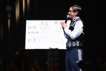 山出愛子と岡田愛の反復横跳び対決の結果を書いたボードと担任の森ハヤシ。