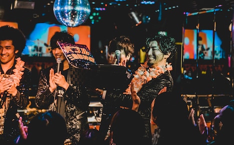 ジャンケンで真行寺貴秋(Vo)に勝利し、“バブル時代の三種の神器”を贈呈される大山聡一(G)。(撮影:ヤマダマサヒロ)