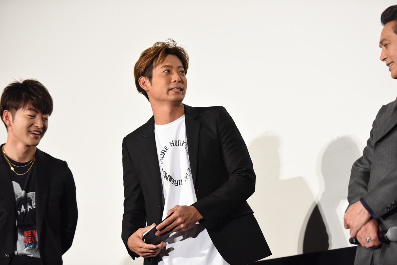 TAKAHIROが達磨に文字を入れる最中、スマートフォンに電話がかかってきて「やべっ、電話鳴っちった！」とあわてる黒木啓司（中央）。