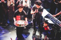 HGYMケーキを持つ岡田梨沙（Dr / ex. D.W.ニコルズ）と拍手する椎名慶治。（撮影：鈴木友莉）